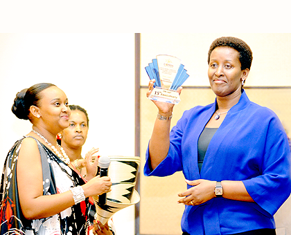 The First Lady, Jeannette Kagame, hoists a plaque of recognition for her support for family and women cause, during the 15th anniversary celebrations for Coopedu, a local micro finance institution, in Kigali yesterday. Left is the Institutions president D