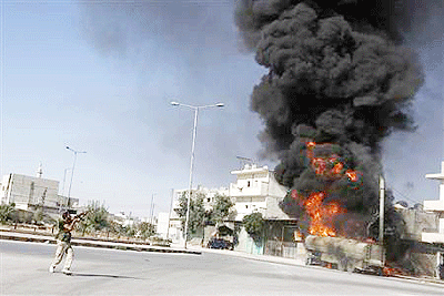 A Free Syrian Army fighter aims his weapon in the air as smoke rises from a petrol tanker that was hit by a missile. Net photo