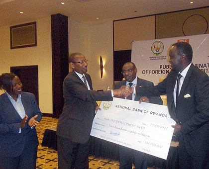 BNR staff representative Thu00e9oneste Bahati (R) hands over a dummy cheque to Finance Minister John Rwangombwa as BNR Governor and Vice Governor, Claver Gatete and Monique Nsanzabaganwa (L), respectively, look on. The New Times/J. Mbonyinshuti.