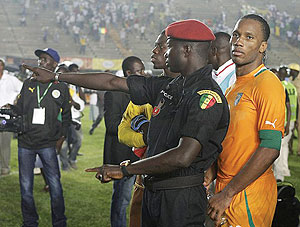 Didier Drogba is shielded by a policeman as trouble rages in the stands. Net photo.