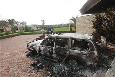 People stand near a burnt car at the U.S. consulate, which was attacked and set on fire by gunmen. Net photo.