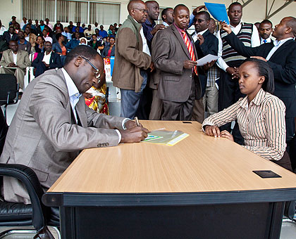 Kigali City Mayor Fidel Ndayisaba sign documents as Liliose Kacoyire of Fraternite De Revelation looks on.  The New Times / T.Kisambira.