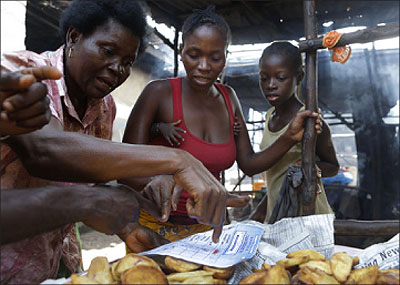 A ruling party supporter from the Mabella slum uses a sample ballot paper to show a neighborhood food vendor how to cast a valid vote for incumbent President Ernest Bai Koroma, in Freetown. Net photo.