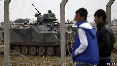 Syrians in the northern town of Ras al-Ain walk near the border fence and a Turkish military vehicle. Net photo