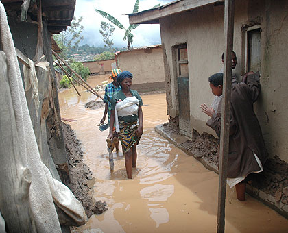 Women wade through flood water in Rwaza last year. Residents evacuated from the area say they need more assistance.  The New Times/ File.