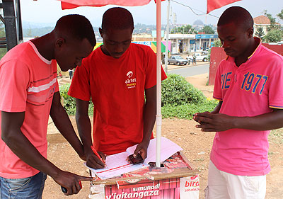 Niyikora (centre) serves a customer. The enterprising youth has been able to fund his education using savings from airtime and airtel money agency sales. The New Times / Ben Gasore