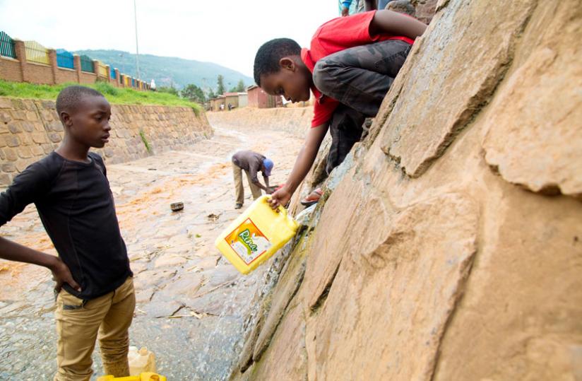 Six-year-old Divin Gatsinzi stretches his hand with a jerrycan to draw water from Kimisagara water channel.