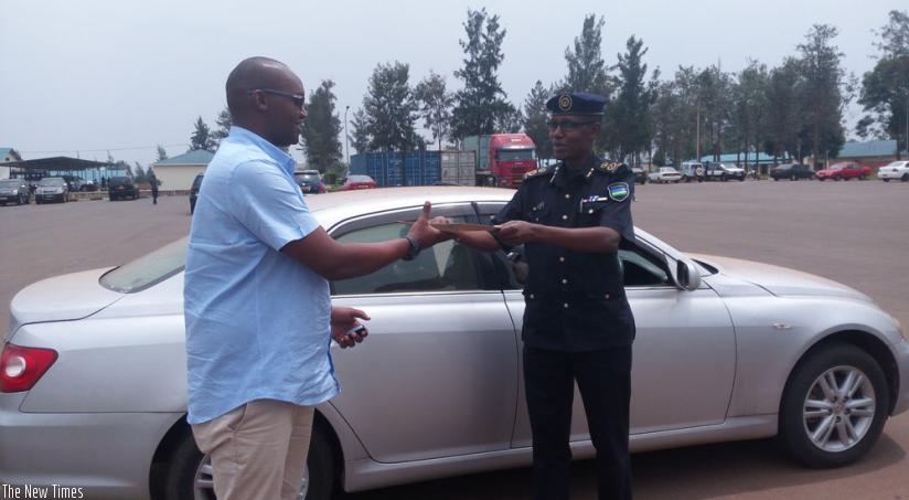 Kananura receives his car documents from ACP Tony Kuramba, the commissioner for Interpol Rwanda, in Kigali, yesterday. (Theogene Nsengimana)